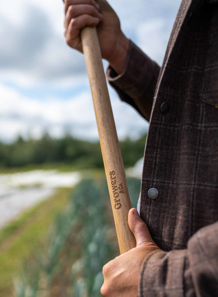 Quelqu'un avec un manche en bois dans lequel est gravé le logo Growers&Co dans les mains.