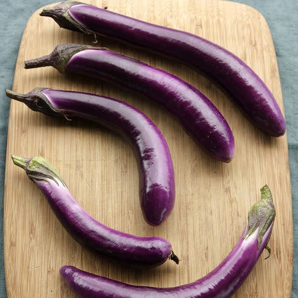 Cinq aubergines longues sur une planche à découper.